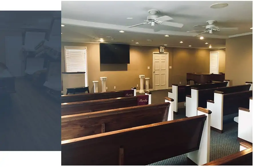 Image description: Peaceful funeral chapel interior with wooden pews facing a modest podium and mounted screen; ceiling fans softly hum above, providing comfort in this serene, carpeted sanctuary. Perfect for respectful cremation services, funerals, and pre-planning events.