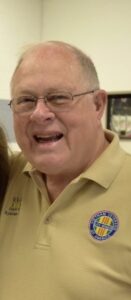 Man wearing glasses and beige logoed polo shirt, smiling indoors for funeral home services promotional image.