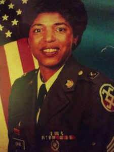 A woman in a U.S. military uniform poses by an American flag for a funeral home honoring Alabama veterans with burial and cremation services.