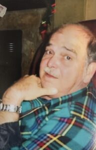 An older man in a plaid shirt sits in a funeral home, reflecting on cremation services in Alabama.