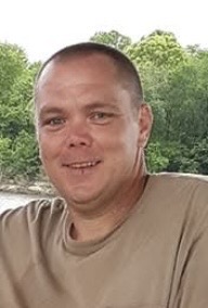 Smiling man in beige T-shirt outdoors, Alabama funeral home cremation services background.