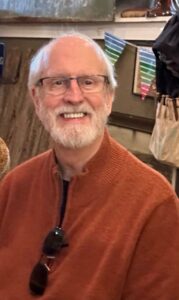 An older man smiles in an orange sweater at an Alabama funeral home event, highlighting funeral costs.