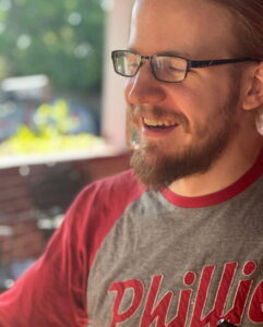 Smiling man in Phillies shirt outdoors, used for Alabama funeral home cremation services.