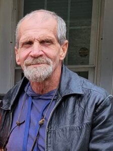 An older man in a black leather jacket stands by a window at an Alabama funeral home.