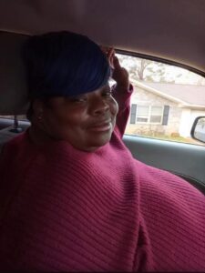 Person in red sweater sits in car outside Alabama funeral home, thinking about cremation services and funeral costs.