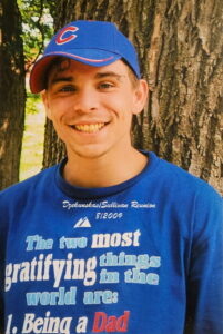 Young man in blue cap and "Being a Dad" shirt at Alabama funeral home, reflecting on cremation services and burial options.