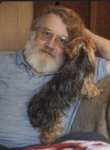 An older man sits on a couch with his dog, reflecting on burial and cremation services in Alabama.