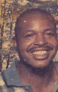 Smiling man with mustache in collared shirt, outdoor scene for Alabama funeral home, cremation services.